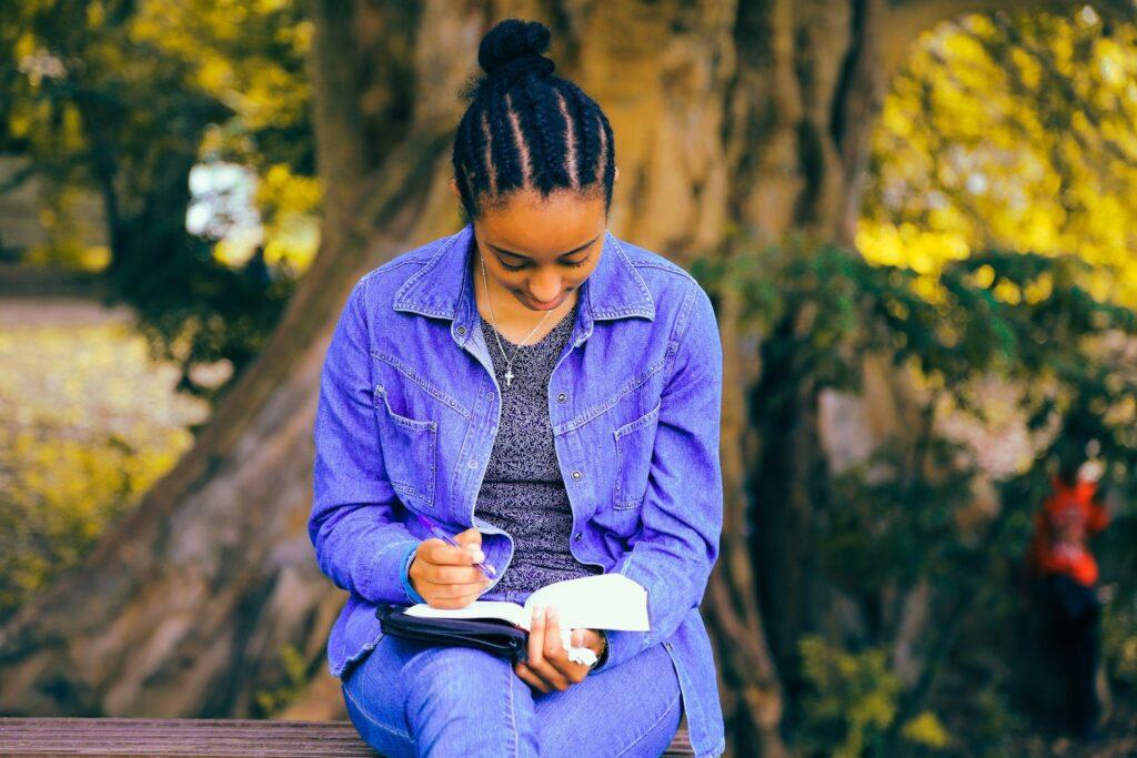 A children's book author writing in a notebook sat in a park