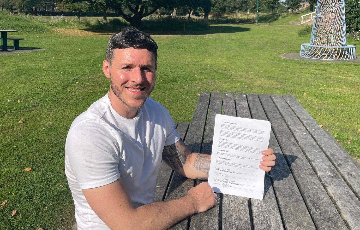 Photo of author Ben Andrews sat on a park bench holding his contract for Better Places